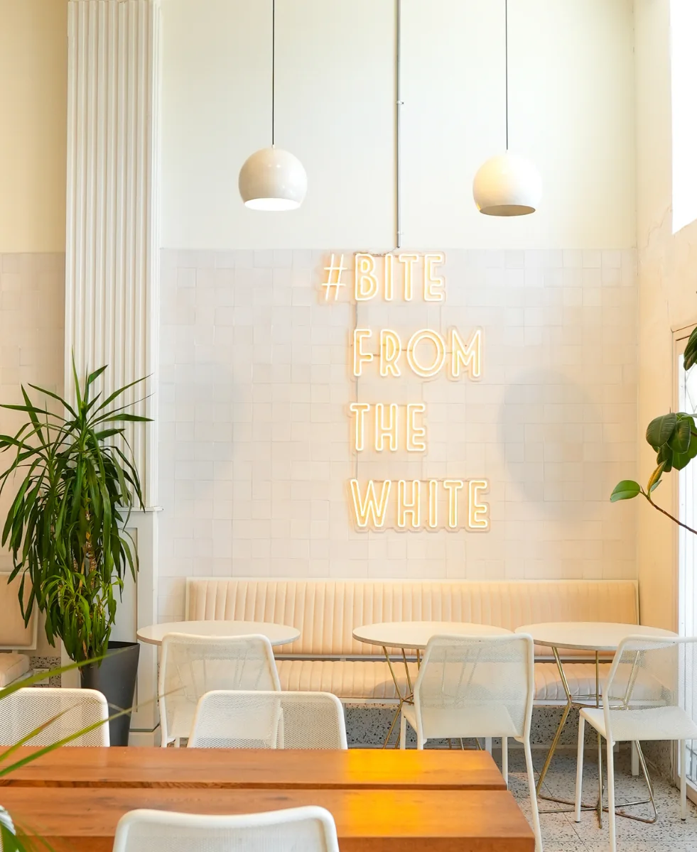 White Burger Yeniköy şubesi: beyaz fayanslı duvarda neon '#BITE FROM THE WHITE' yazısı, sarkıt lambalar, bitkiler ve ahşap masa